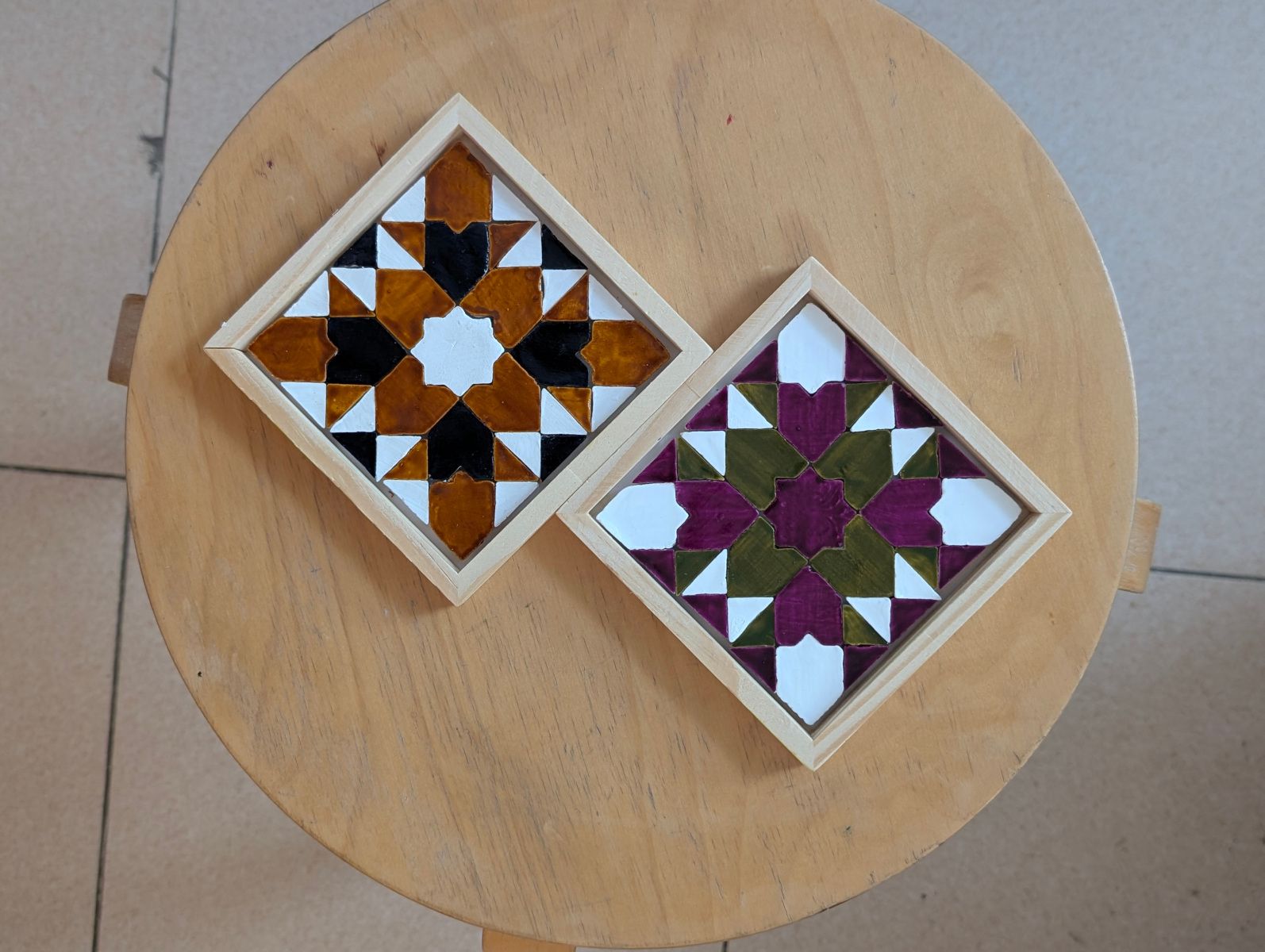 Twee afgewerkte geometrische mozaïekonderzetters op een ronde houten kruk
